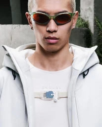 Close-up portrait of a male model wearing tinted sunglasses, white t-shirt and light grey zip hoodie for Oakley