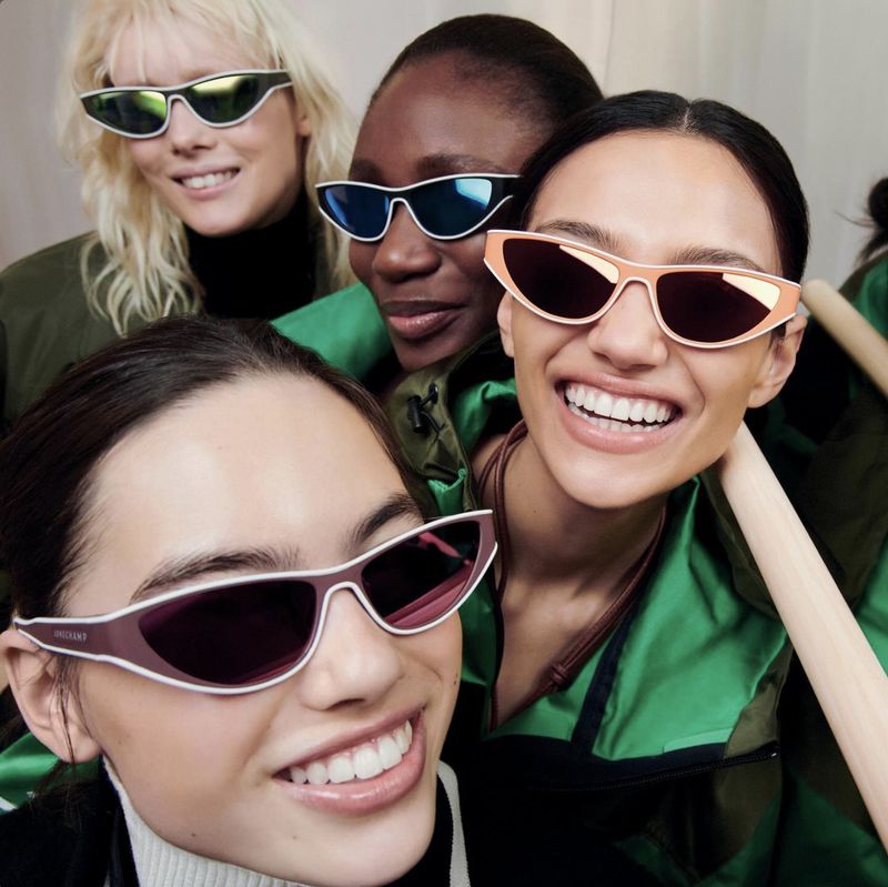 A group of four diverse women smiling and wearing fashionable sunglasses in a close-up, capturing a blend of style and positivity.