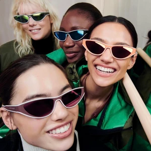 Four models wearing cat-eye sunglasses and green outerwear smiling together for Longchamp Team Spirit.
