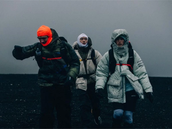 Three people in winter clothing walking on a black sand beach on a foggy day, with focus on the people and their outdoor attire.