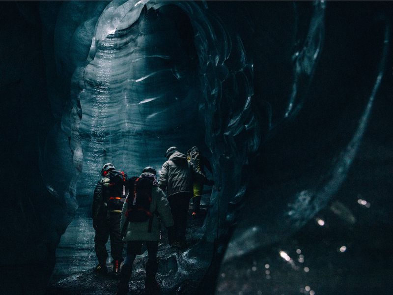 Group of people explores a blue ice cave with textured walls and dark interior, creating a sense of adventure and exploration in nature.