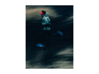 A runner in motion captured with long exposure blur wearing a light jacket and bright orange headband against a dark blurred outdoor terrain