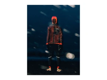 A runner wearing an orange hooded jacket and black running tights standing outdoors during falling snow at night for Adidas Terrex.