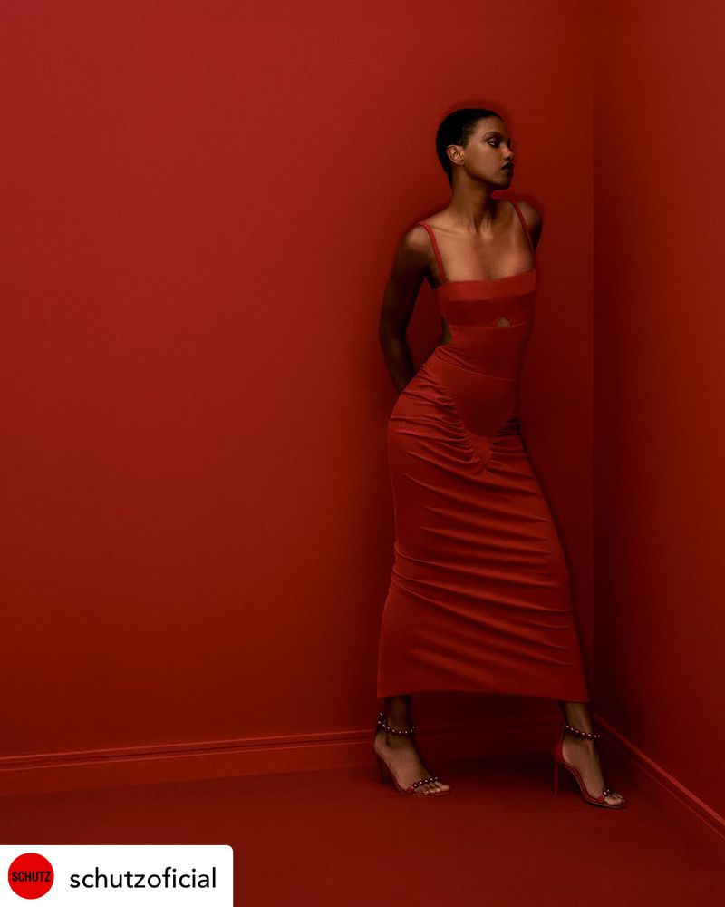 Elegant woman in a red dress poses in a photo studio with a matching red backdrop, highlighting fashion and studio photography.