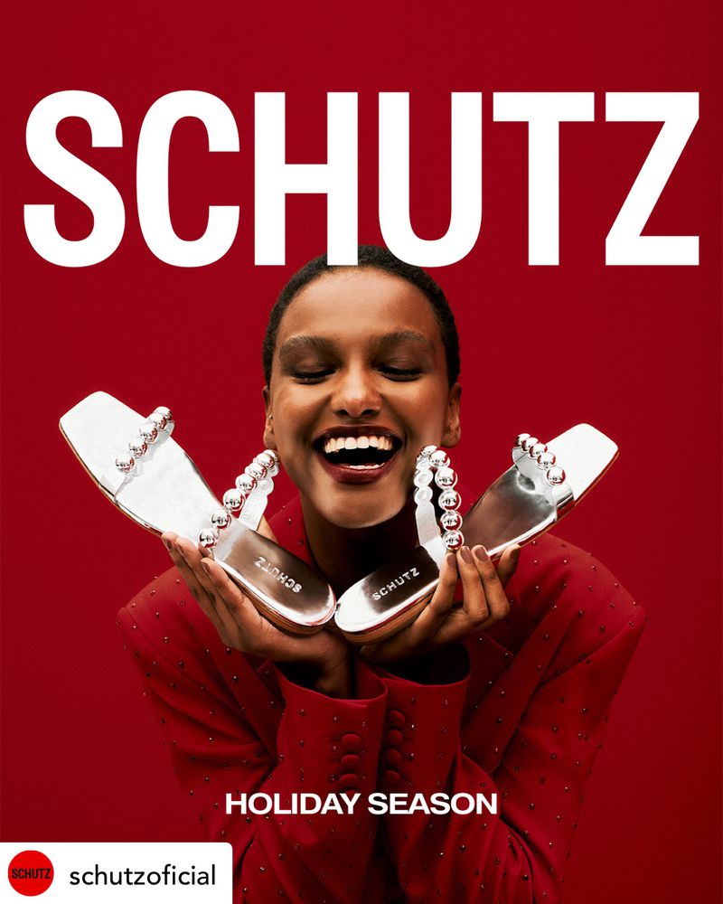 Fashion-forward ad featuring a smiling woman holding silver high-heeled sandals against a vibrant red backdrop, showcasing Schutz shoes.