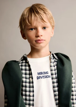 Young boy with blonde hair wearing a plaid shirt over a white t-shirt with text against a grey background