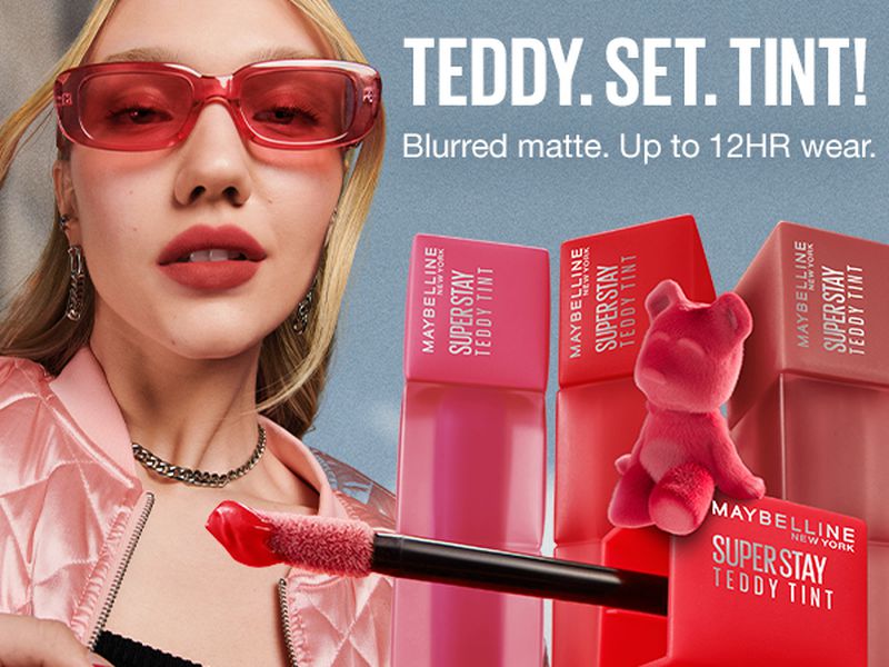 Beauty shot showcasing Maybelline Super Stay Teddy Tint lipstick with a fair-skinned woman wearing pink sunglasses and a pink jacket.