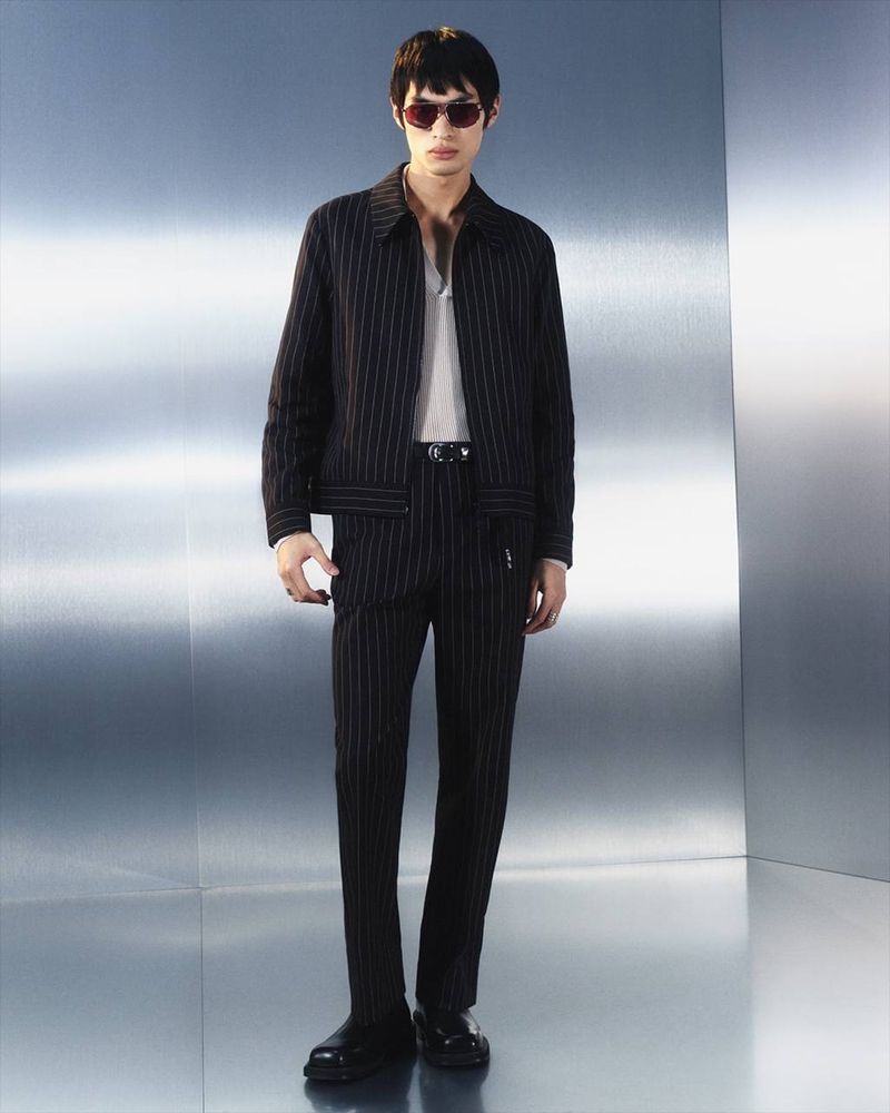 Adult male in pinstripe suit with sunglasses posing against a modern, silver background in a studio setting for a fashion editorial.