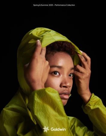 Close-up of a young adult female in a bright green hooded jacket, photographed against a dark background. Fashion shot of apparel.