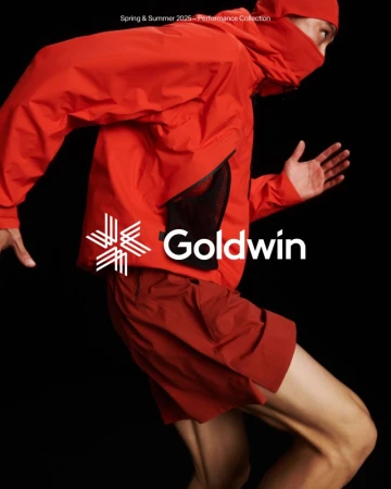 Person in motion wearing a red Goldwin hooded jacket and shorts against a black backdrop, showcasing athletic apparel.
