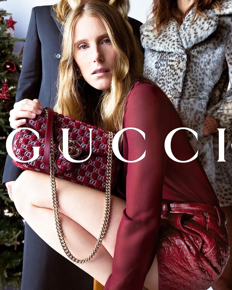 Fashion editorial featuring a female model in a red outfit, kneeling with a Gucci handbag, alongside other models in the background.