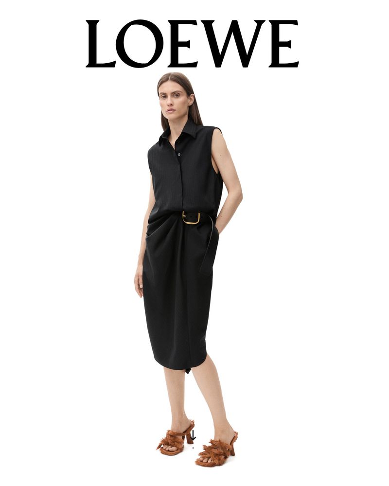 Fashion editorial shot: A woman in a black dress and brown heels posing against a white background in a studio with dramatic lighting.