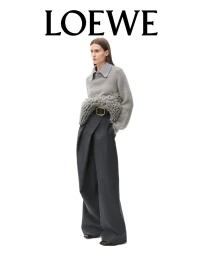 Model standing against a white backdrop wearing a grey textured sweater and wide-leg dark trousers for Loewe FW24