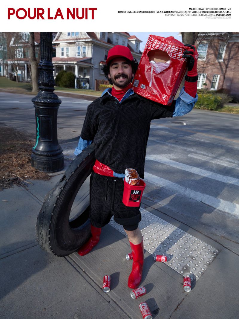Man in red hat poses with tire and shopping bag near buildings and street lamp with soda cans scattered on sidewalk.
