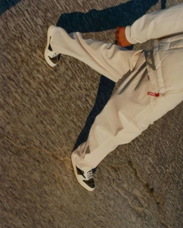 Person in white pants and black-and-white sneakers stands on mottled grey surface with sharp shadow. Fashion and style concept.