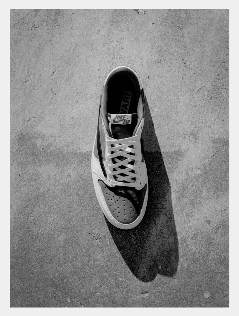 Top-down shot of a single black and white Nike sneaker with white laces casting a shadow on a grey concrete surface.