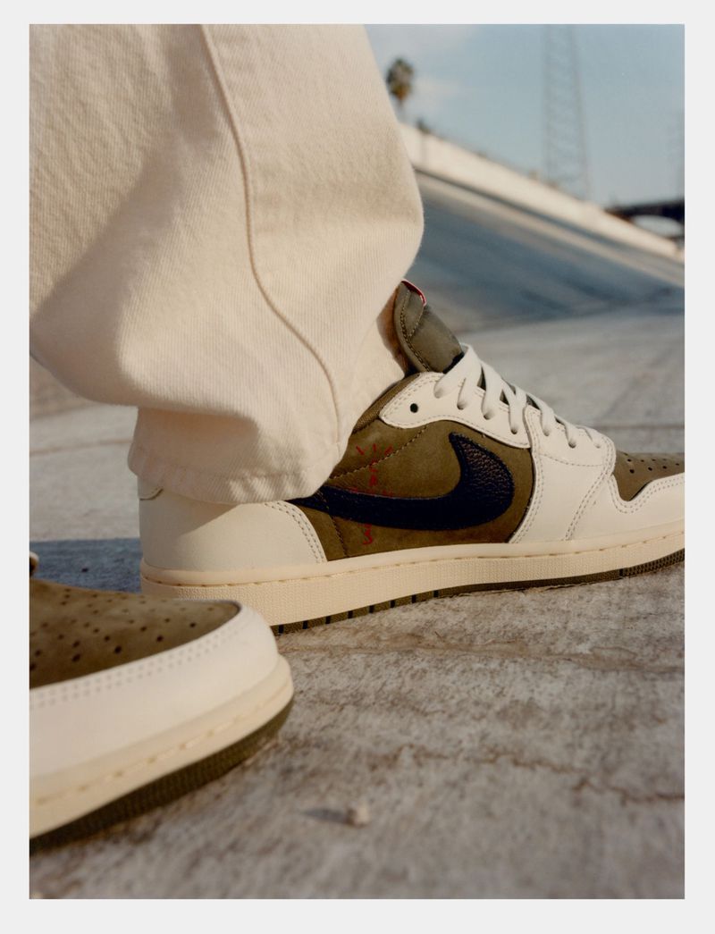 Close-up of khaki and white sneakers with a black swoosh on concrete; one sneaker is partially visible in the foreground.