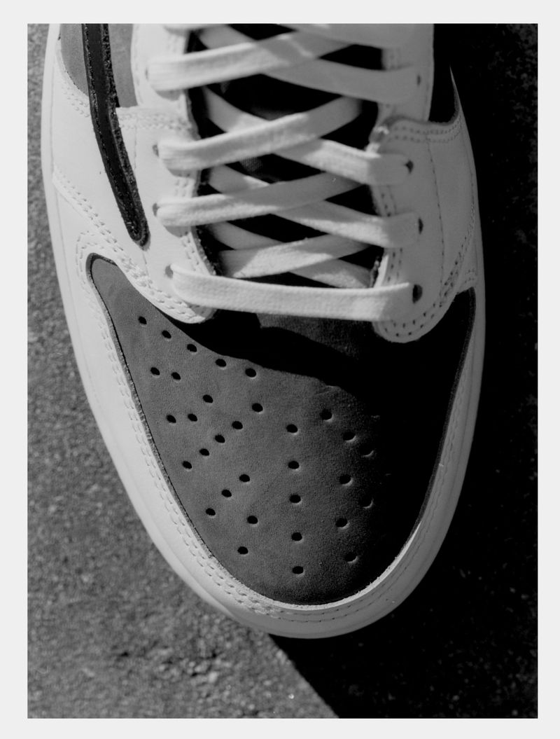 Close-up of a black and white sneaker featuring white laces, a toe box with perforations, and a textured background.