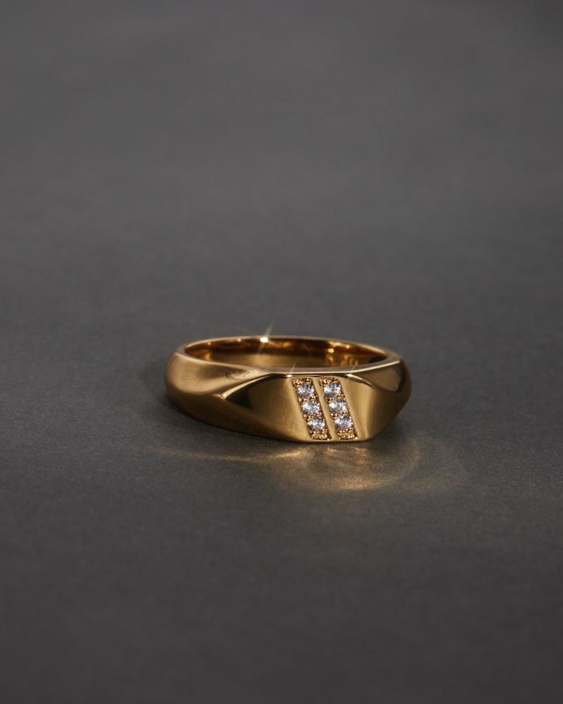 Close-up studio shot of a gold ring with diamonds. The ring is centered and well-lit against a dark gray background.