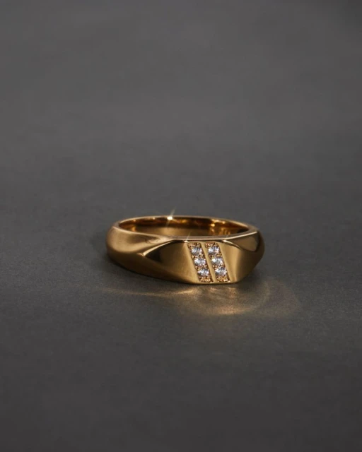Close-up studio shot of a gold ring with diamonds. The ring is centered and well-lit against a dark gray background.