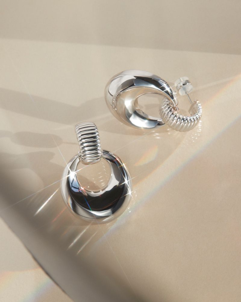 Close-up studio shot of a pair of silver-colored earrings with a modern design, showcasing their reflective surface and smooth curves.
