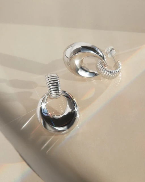 Close-up studio shot of a pair of silver-colored earrings with a modern design, showcasing their reflective surface and smooth curves.