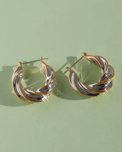 Close-up studio shot of a pair of metallic twisted hoop earrings with white and gold tones against a muted green background.