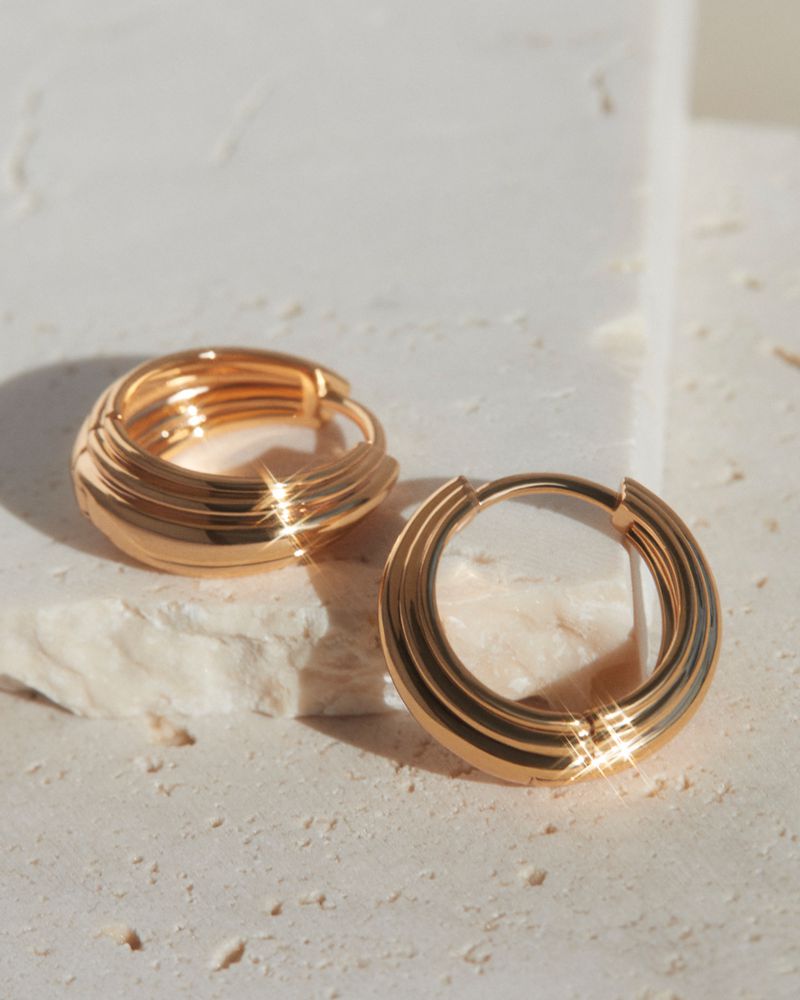 Close-up studio shot of gold hoop earrings. Jewellery product photography displays elegant earrings on neutral surface with soft, diffused lighting.