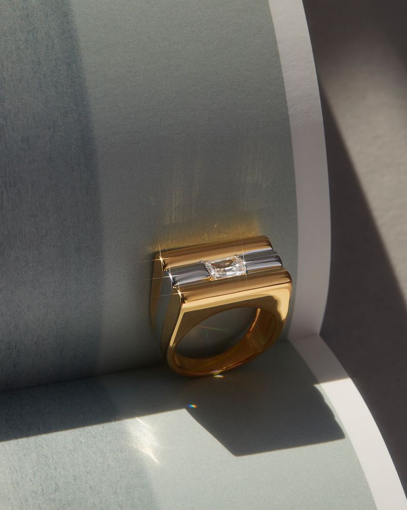 Elegant gold ring with a rectangular design and a central clear stone, highlighted by a soft, diffused light that enhances its luster.