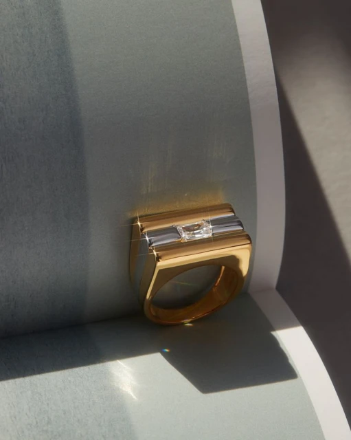 Elegant gold ring with a rectangular design and a central clear stone, highlighted by a soft, diffused light that enhances its luster.