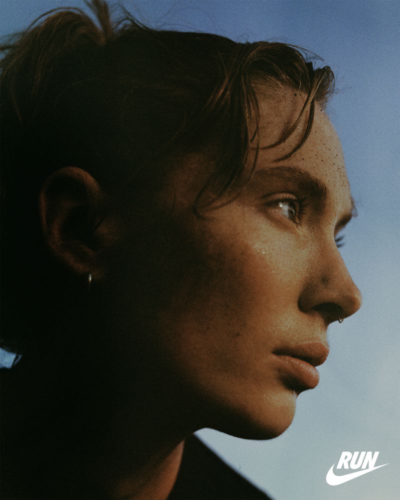 Portrait of an adult female with freckles and facial piercings looking off into the distance with a blue gradient sky background.