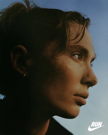 Portrait of an adult female with freckles and facial piercings looking off into the distance with a blue gradient sky background.