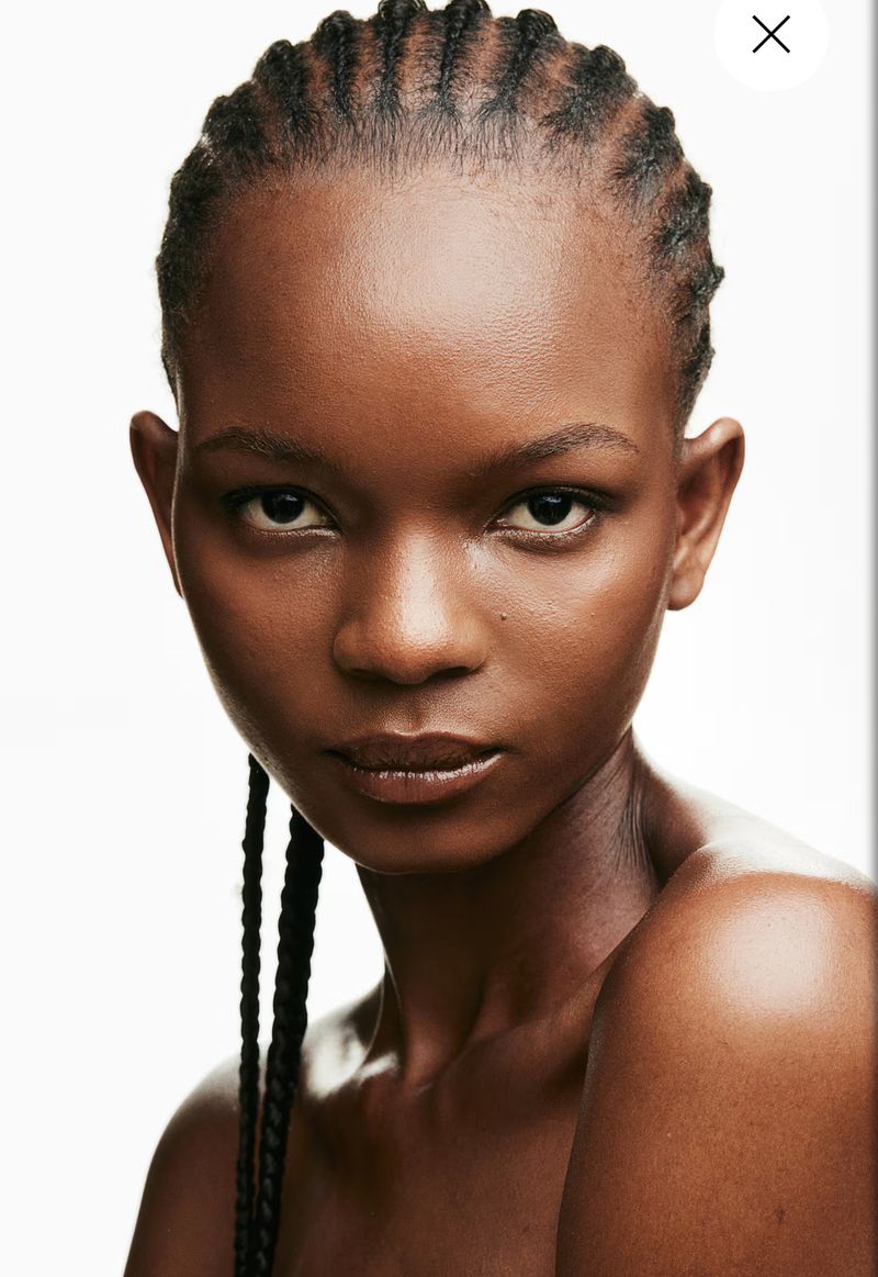 Close-up beauty shot of an African woman with braided hair in a studio setting, showcasing her skin tone and hair texture against a clean background.