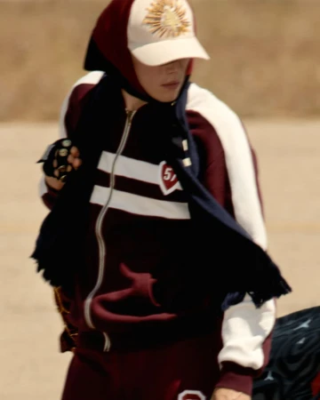Stylish person in a maroon and white tracksuit with a cap poses outdoors, showcasing fashion and urban style against a neutral backdrop.