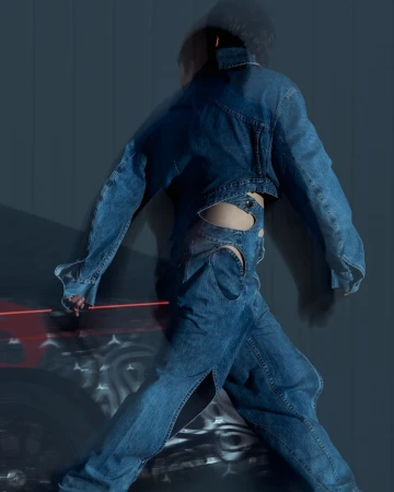 Fashion shot of person wearing cut-out denim jacket and jeans, walking against a blurred background with red light streaks. 