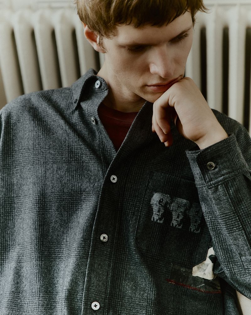 Portrait of an adult male wearing a grey plaid collared shirt with elephant graphic design inside an indoor environment.