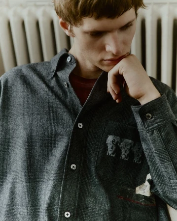 Portrait of an adult male wearing a grey plaid collared shirt with elephant graphic design inside an indoor environment.