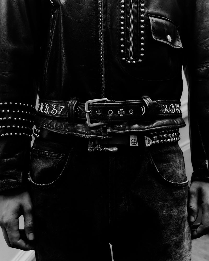 A close-up in black and white shows a man wearing a studded leather jacket and multiple belts, with Japanese text visible on one belt.