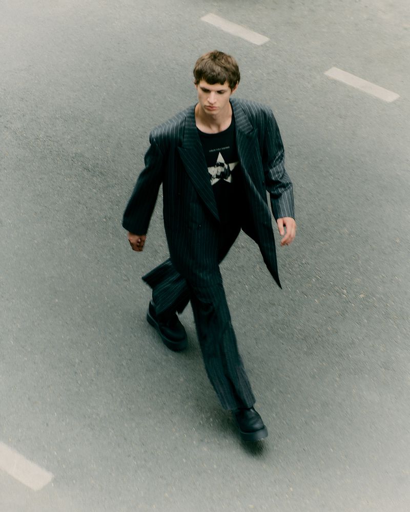 Male fashion model walks on a city street wearing a pinstripe suit and t-shirt. Overhead shot.