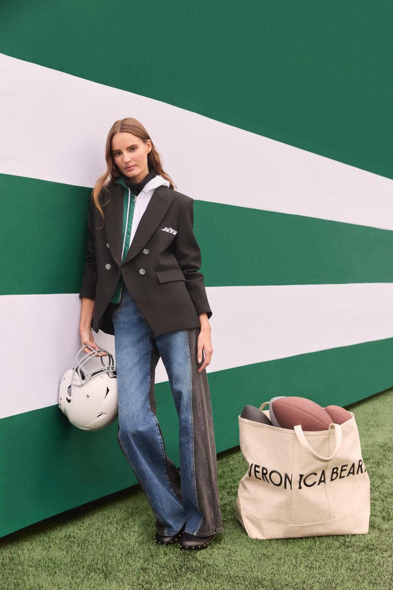 A fashionable woman poses in a blazer and jeans with an American football helmet and bag on a green and white striped background.