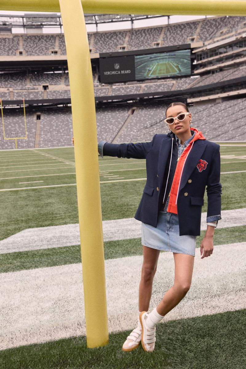 A person models a blazer, hoodie, and denim skirt on a football field next to a goalpost, creating a sporty and stylish aesthetic.