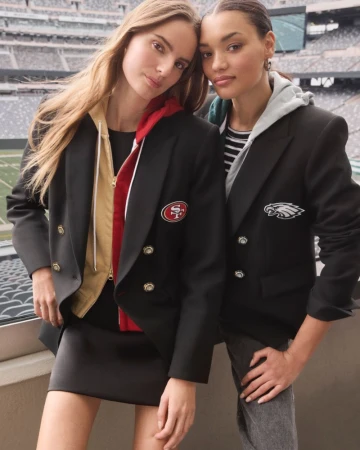 Two women posing in football jackets with stadium background. Fashionable outfits. San Francisco 49ers and Philadelphia Eagles attire.