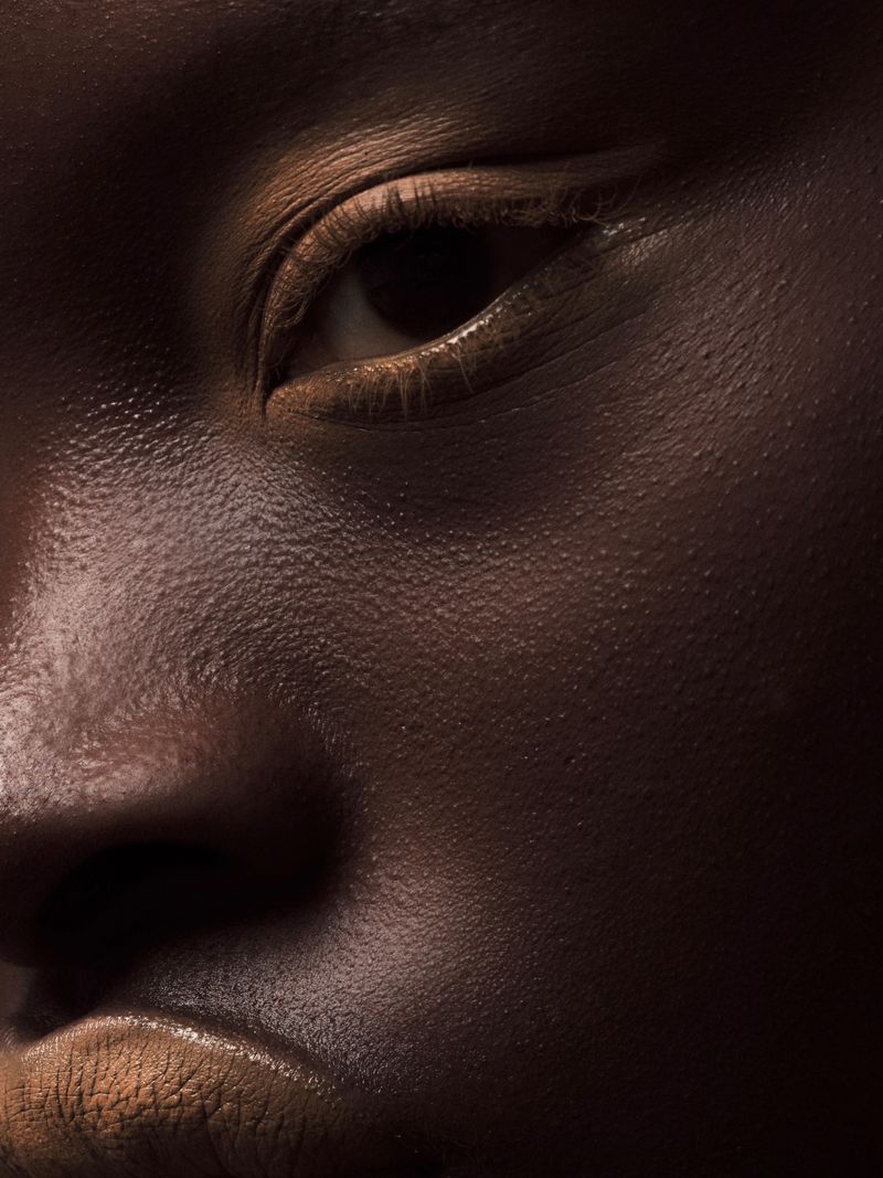 Close-up portrait of an adult female with brown skin in a studio setting, focusing on the skin's texture and the model's eye.