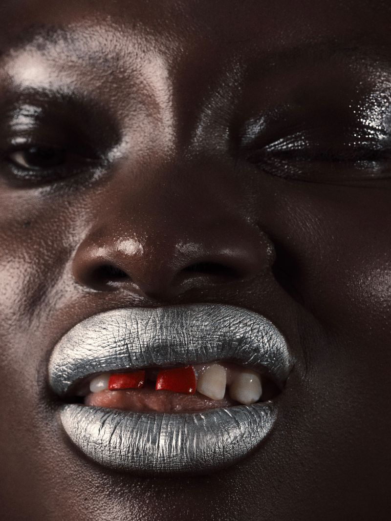 Close-up portrait of a dark-skinned person with silver lipstick and a slight grimace, emphasizing beauty and facial expression.