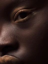Extreme close-up beauty portrait of a Black model featuring detailed skin texture and neutral makeup accents on the eyes and lips.