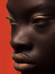 Close-up portrait of a Black woman with metallic gold eyeliner against a vibrant red background for Schön Magazine.