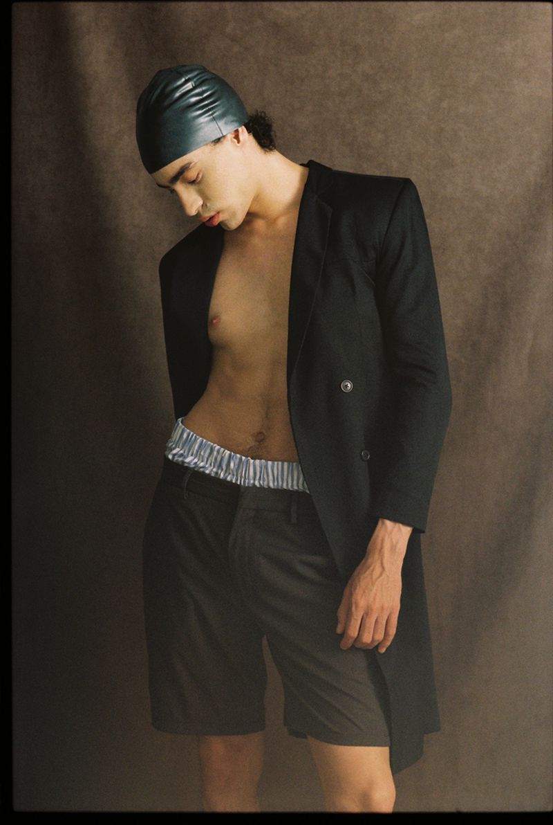 Person with a swim cap and blazer in a studio setting. The model is posing and looking down with brown background.