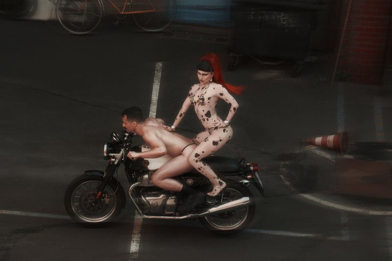 Two people on a motorcycle on a dark asphalt road. The woman wears a spotted bodysuit with red hair. A vintage bicycle is visible.