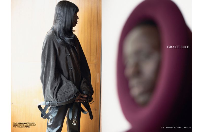 Editorial fashion shot featuring two women with dark hair. One is in a dark coat with belts. The other is wearing a hooded garment.