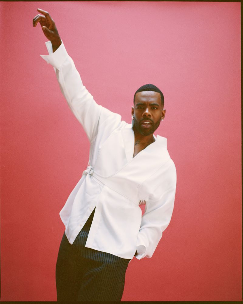 Portrait of a Black man in a white shirt posing against a pink background, with one arm raised in a bright and colorful composition.